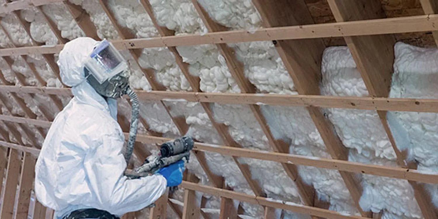 Technician spraying foam between attic rafters